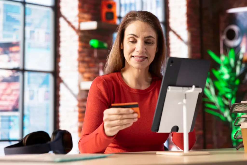 Smiling woman holding a credit card while making an online purchase on a tablet, highlighting a seamless e-commerce shopping experience.